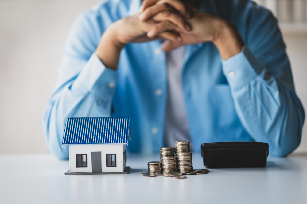 Uomo preoccupato davanti a casa in miniatura e soldi: mutuo non pagato e rischio pignoramento